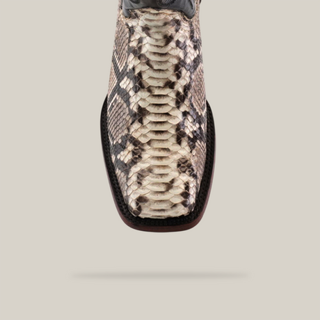 Close-up view of the Exotic Python - Natural boot, featuring a luxury snakeskin pattern in cream, brown, and black. The handcrafted cowboy boot with a rodeo toe is set against a plain beige background.