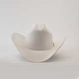 The 6X Real White is a luxury Western cowboy hat with a wide brim and creased crown, handcrafted by artisans from fur felt. It is elegantly displayed against a plain white background.