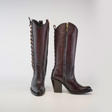 A pair of Francia Rings Tall Shaft Chocolate boots crafted from premium leather, with block heels and side zippers. The left boot is front-facing, while the right showcases a decorative chain along the back, embodying sleek elegance.