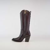 The Francia Rings Tall Shaft Chocolate - J Toe boot is crafted from premium leather, featuring a tall, chocolate silhouette with a side zipper and decorative back stitching. Its pointed toe and chunky heel embody understated luxury against a plain white background.