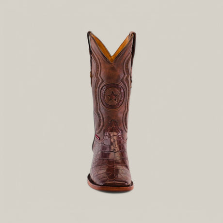 A single brown cowboy boot, crafted from Exotic American Alligator Belly, features intricate stitching and a central star emblem, displayed against a plain backdrop.