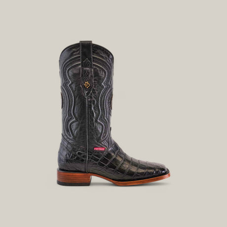 The Exotic American Alligator Belly boot in black boasts Western craftsmanship with intricate stitching, crocodile texture, a wooden heel, a square toe design, and a small logo tag near the sole against a light gray background.