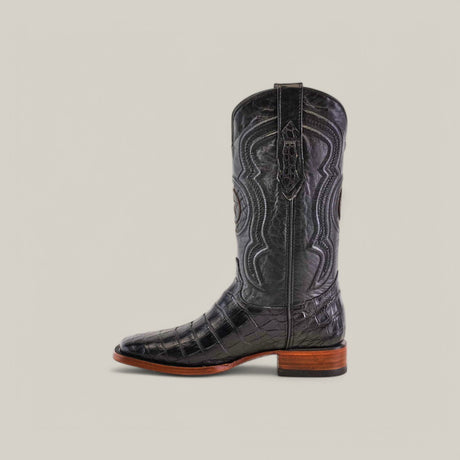 The Exotic American Alligator Belly - Black - Square Toe boot exhibits Western craftsmanship with intricate stitching, a textured surface, and a brown wooden heel. Set against a plain beige background, it features detailed patterns along the shaft and a slightly square toe design.