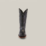 Front view of Exotic American Alligator Belly boots in black, showcasing a square toe, intricate patterns, and a circular emblem on the shaft. These Western-crafted boots feature a dark brown sole set against a plain gray background.