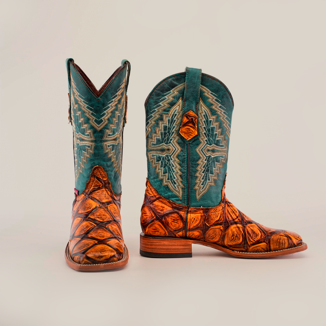 The Big Bass Pirarucu Print Tan - Square Toe is a handcrafted cowboy boot featuring a textured cowhide leather foot with detailed patterns, a tall teal shaft with intricate embroidery, a flat heel, and a smooth sole.