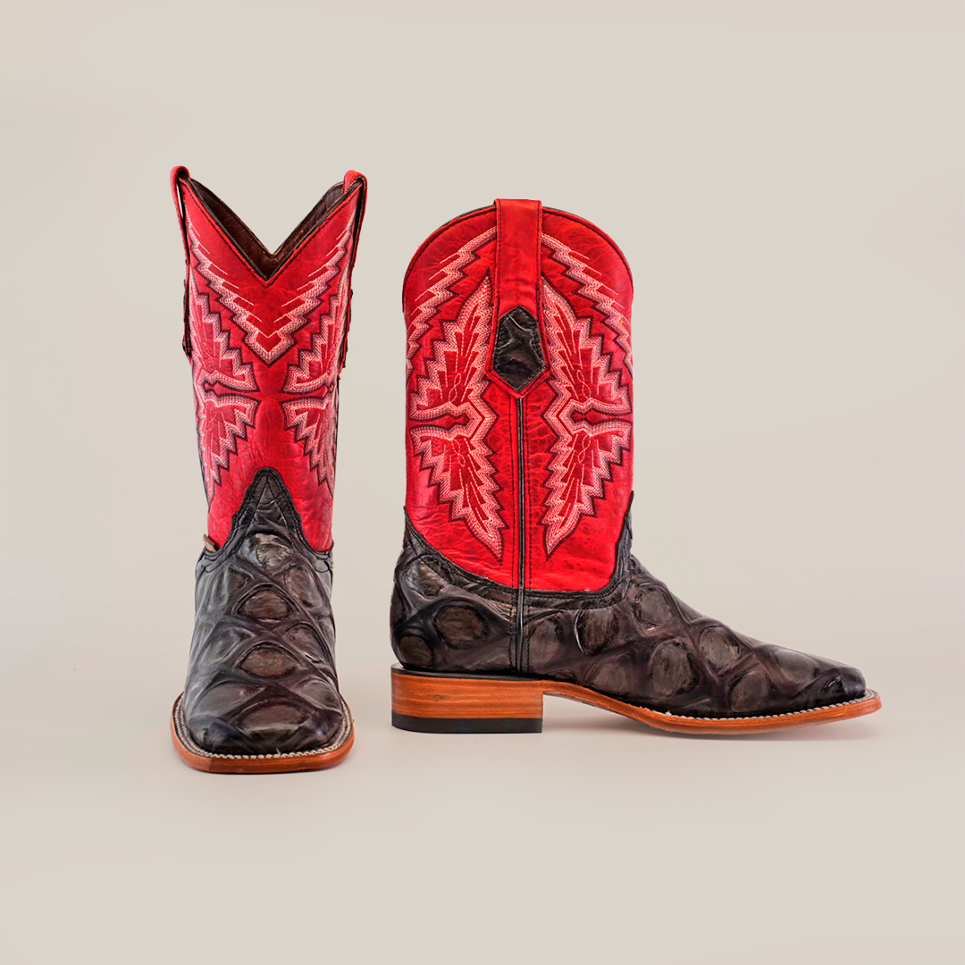 The Big Bass Pirarucu Print Rustic Black boots feature a dark brown textured lower section with vibrant red intricately stitched upper shafts, crafted from premium cowhide leather. These square toe boots with wooden heels stand out elegantly against a plain white background.