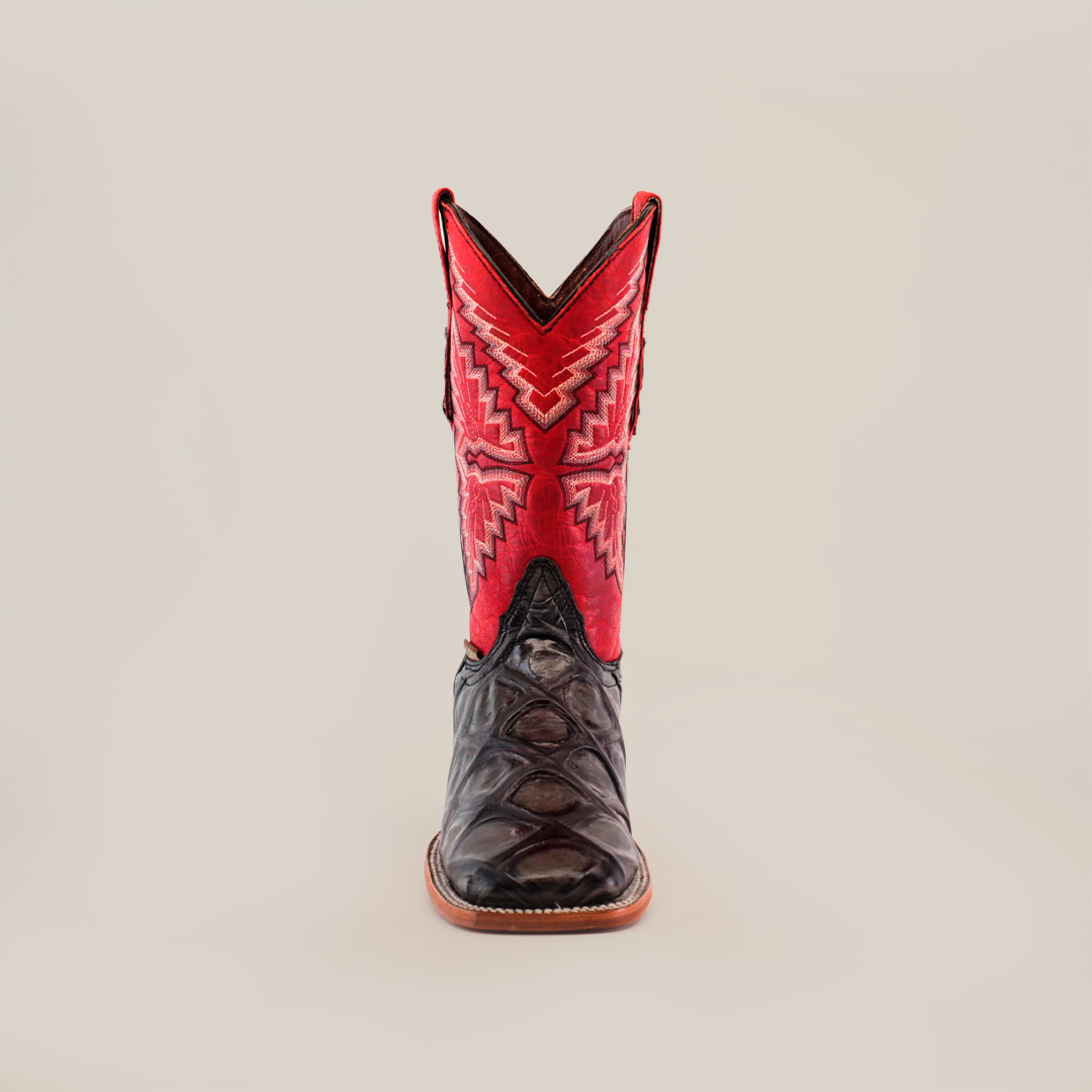 The Big Bass Pirarucu Print Rustic Black boot features a premium cowhide with a dark brown foot, a tall shaft in vibrant red and pink zigzag, and a square toe for style. The tan sole ensures it stands upright against the white background.