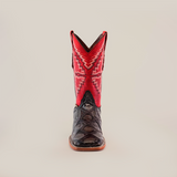 The Big Bass Pirarucu Print Rustic Black boot features a premium cowhide with a dark brown foot, a tall shaft in vibrant red and pink zigzag, and a square toe for style. The tan sole ensures it stands upright against the white background.