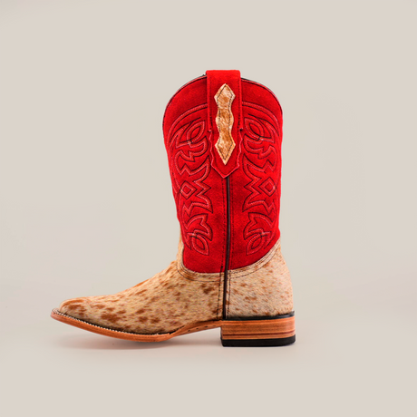 Introducing the Cowhide Hair Red Suede Shaft Pinto - Square Toe: This cowboy boot features a tan speckled cowhide leather foot and a vibrant red suede shaft adorned with intricate stitching and a decorative beige inlay. It boasts square toe styling, complemented by a wooden heel on a plain white background.