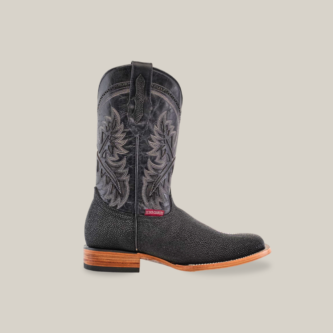 The image features the King Stingray Print Black - Square Toe, a handcrafted black cowboy boot with premium cowhide leather, intricate stitching, and a slightly pointed toe. It has a brown wooden heel and a tag near the ankle on a plain white background.