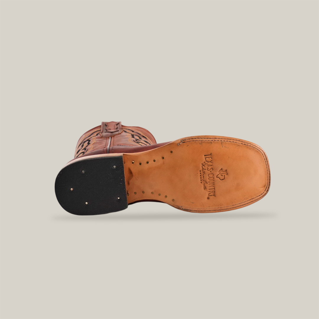 The Fresno Shedron - Square Toe cowboy boot features a brown leather sole view, detailed stitching, and Tecovas logo. Made from premium cowhide leather, it has a reinforced heel with black material and metal studs. The plain white background emphasizes its expert craftsmanship.