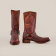 A pair of handcrafted Azkar Moka brown leather boots, designed with a slip-resistant sole and biker toe, are displayed on a plain white background. One boot faces forward and the other to the side, showcasing their harness design and decorative stitching.