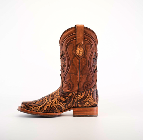 The Handtooled Leave Orix boot, crafted from premium cowhide leather, features intricate embossed patterns and detailed stitching. With a low wooden heel and slip-resistant sole, it combines traditional Western style with practicality against a white background.