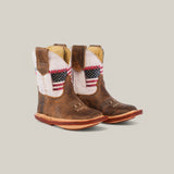 Scott Camel USA Shaft Square Toe Baby Boots are brown cowboy boots for toddlers with an American flag design, stars and stripes on the sides. They feature premium materials, light stitching, and a wooden sole over a simple backdrop.