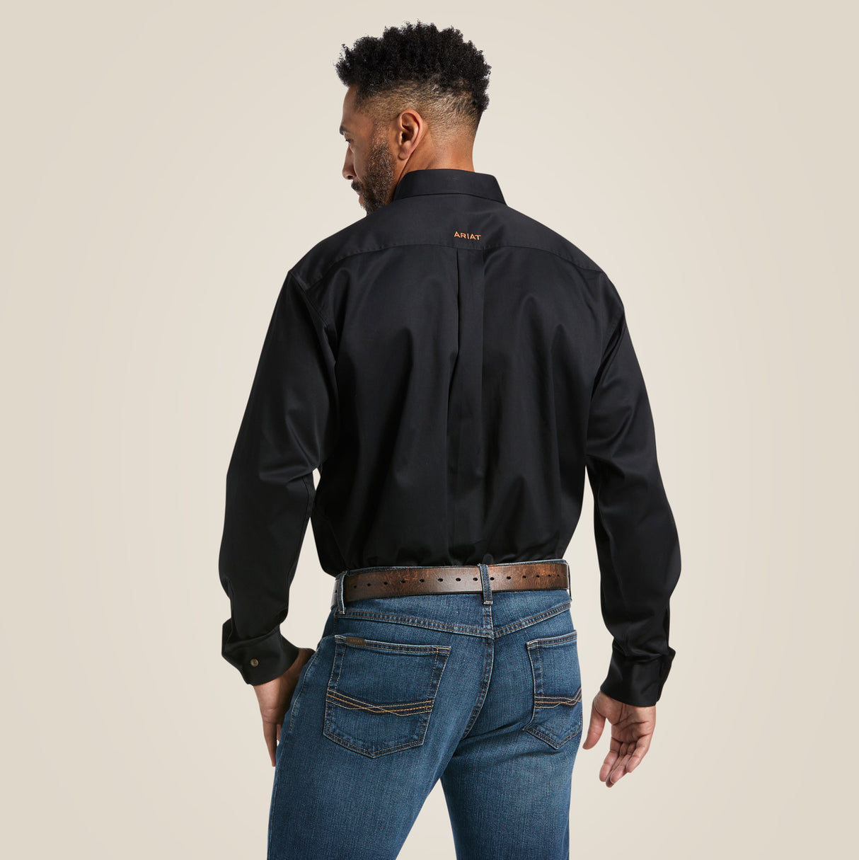 A man in a Solid Twill Classic Fit Shirt Black (10000502) and blue jeans is seen from behind. The shirts classic fit includes embroidered details with a brand logo on the upper back. He stands against a plain, light-toned backdrop.