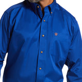 A person with a beard, face not visible, wears a bright blue Solid Twill Classic Fit Shirt (Product: 10006660) featuring a collar and chest pocket with an emblem, made from 100% Cotton Twill.