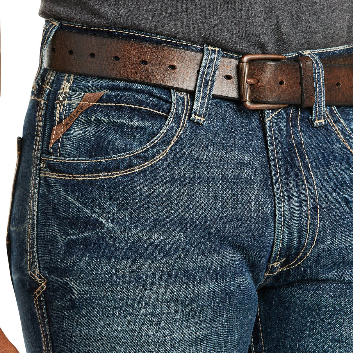 Close-up of a person wearing M5 Slim Boundary Stackable Straight Leg Jeans, Gulch - 10014010, featuring blue denim with contrast stitching, a small pocket with leather tag, paired with a brown leather belt and dark gray shirt.