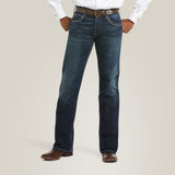 A person wearing a white shirt and M5 Slim Stretch Coltrane Stackable Straight Leg Jean - Nightingale stands against a plain background. The jeans, with reinforced pockets and slight fading, are complemented by a brown belt and brown leather shoes.