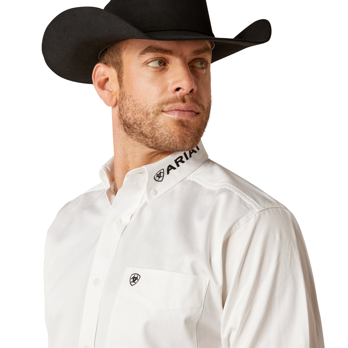 A bearded man looks to the side wearing a black cowboy hat and the Team Logo Twill Classic Fit Shirt White (10046825) by ARIAT. The shirt features ARIAT on the collar, embroidered details, and a small chest logo.