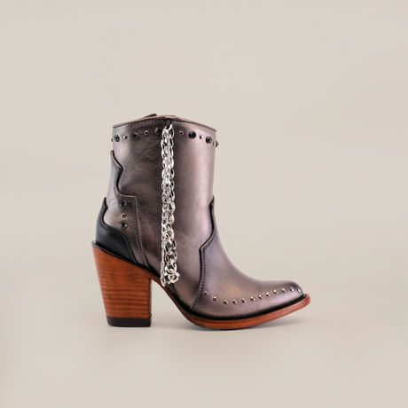 The handcrafted Milan Chains Bootie Silver - J Toe features a metallic gray finish with decorative silver chains and studs, complemented by a wooden block heel and dark accents, making it an ideal statement piece from the Platinum Collection.