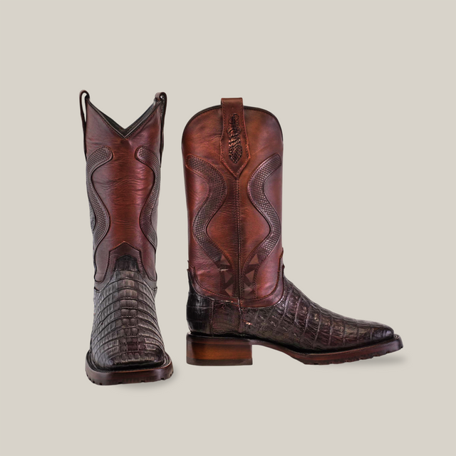 The Exotic Caiman Belly Tail - Diamond - Tabaco boots feature dark brown caiman belly tail leather with intricate shaft stitching. One boot stands upright while the other tilts to reveal its side and toe designs, set against a light background with a durable Goodyear welt double sole.