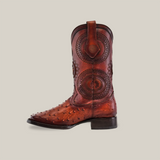 A single brown cowboy boot, from the coveted Platinum collection, features intricate circular patterns and decorative studs on the toe. This embodies cowboy culture with its Ostrich Honey Square Toe design set against a plain background.