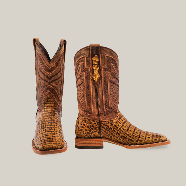 A pair of Exotic Caiman Horn Back - Antique - Square Toe boots is displayed, showcasing intricate leather detailing and genuine caiman leather with a textured, crocodile-like appearance. One boot is front-facing while the other is side-facing against a plain beige background.