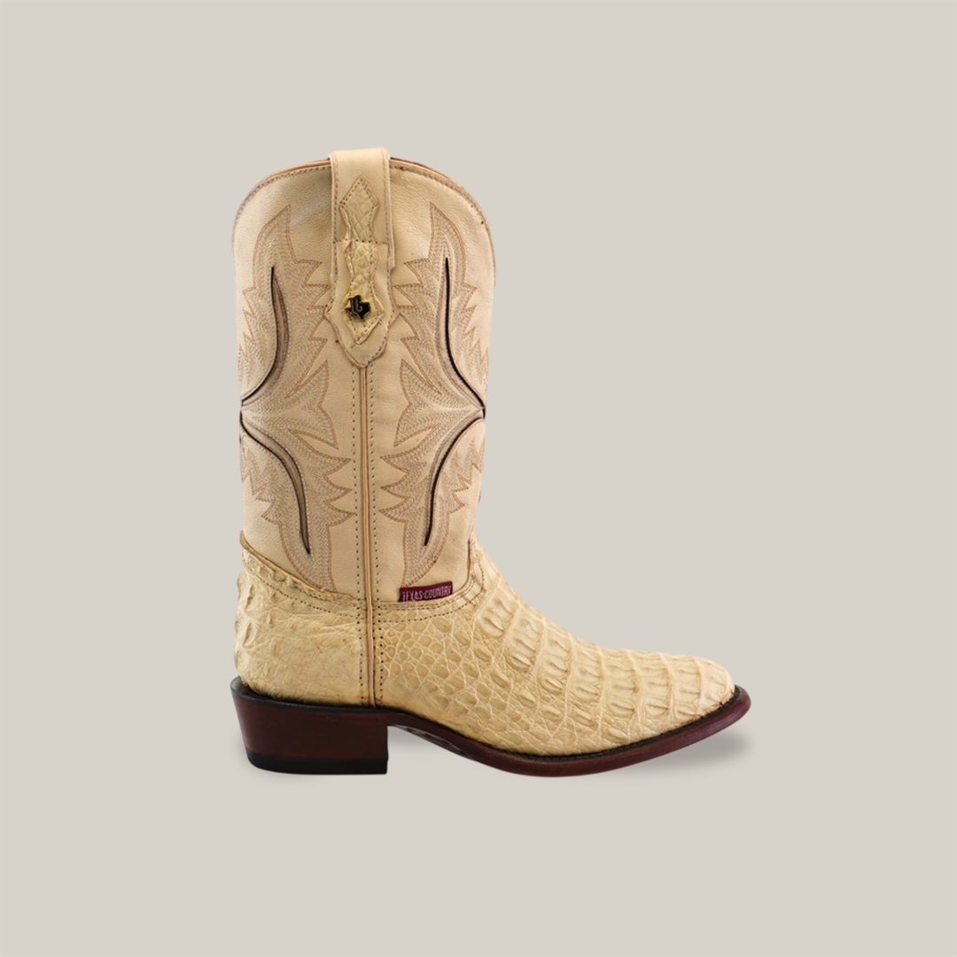 The Exotic Caiman Hornback in bone features a single beige cowboy boot crafted from authentic caiman leather with intricate stitching, textured surface, and decorative pull loop. Its elegant design is enhanced by a wooden heel and sole, displayed on an off-white background.