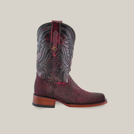 The Exotic Stingray Wine boot features a luxurious stingray leather upper with intricate dark designs, decorative stitching, a rich red-brown texture, a rodeo toe, and a wooden heel, all set against a plain light grey background.