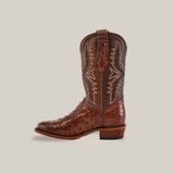 The Exotic Full Quilt Ostrich Brown Round Toe boot, with a textured surface and decorative stitching, showcases leather artistry. This handcrafted single cowboy boot features a low heel and pull straps against a plain, light beige background.