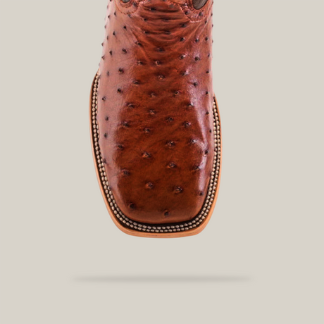 Close-up of the Exotic Full Quilt Ostrich - Brandy boot, featuring ostrich leather texture and a square toe. Detailed stitching defines its essence against a plain, light backdrop.