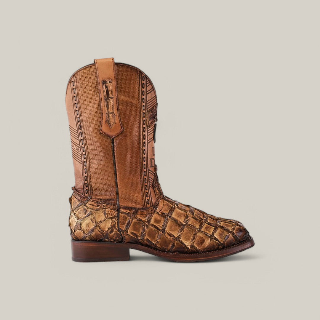 The Asturias Honey Fish Pirarucu Laser & Woven - Square Toe - CU658 is a single cowboy boot crafted from brown leather with a textured design, intricate stitching on the laser-engraved shaft, and a distinct snakeskin pattern vamp made of Pirarucu fish leather. It includes a low heel and pull straps.