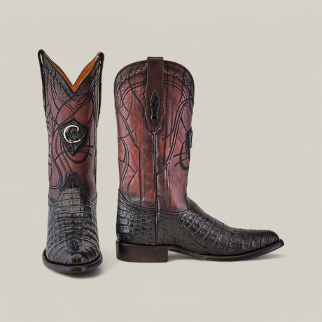 The Plunge Black Caiman Laser & Embroidery - Round Toe boots feature ornate designs using luxurious Caiman leather: the left boot displays black and brown patterns from the front, while the right shows a side view with a laser-engraved leaf motif, complemented by a rich leather texture.