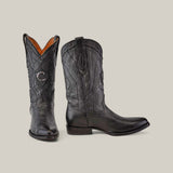 The CU682 cowboy boots, made from black deer leather, showcase intricate laser-engraved patterns. One boot stands upright and the other lies on its side, revealing the design and heel against a plain light gray background.