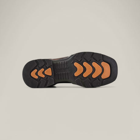 The image displays the underside of the Taurus Honey Composite Toe - E6189 boot, featuring a black outsole with orange chevron-shaped grips. This unique tread pattern enhances traction and durability, while the plain background accentuates the boots robust design.