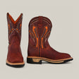 The Floter Shedron Soft Toe - E6987 features brown leather cowboy boots with intricate orange stitching. The left boot is angled to display the toe, while the right shows a side view. These boots boast a black sole and thick beige heel, offering both style and durability.