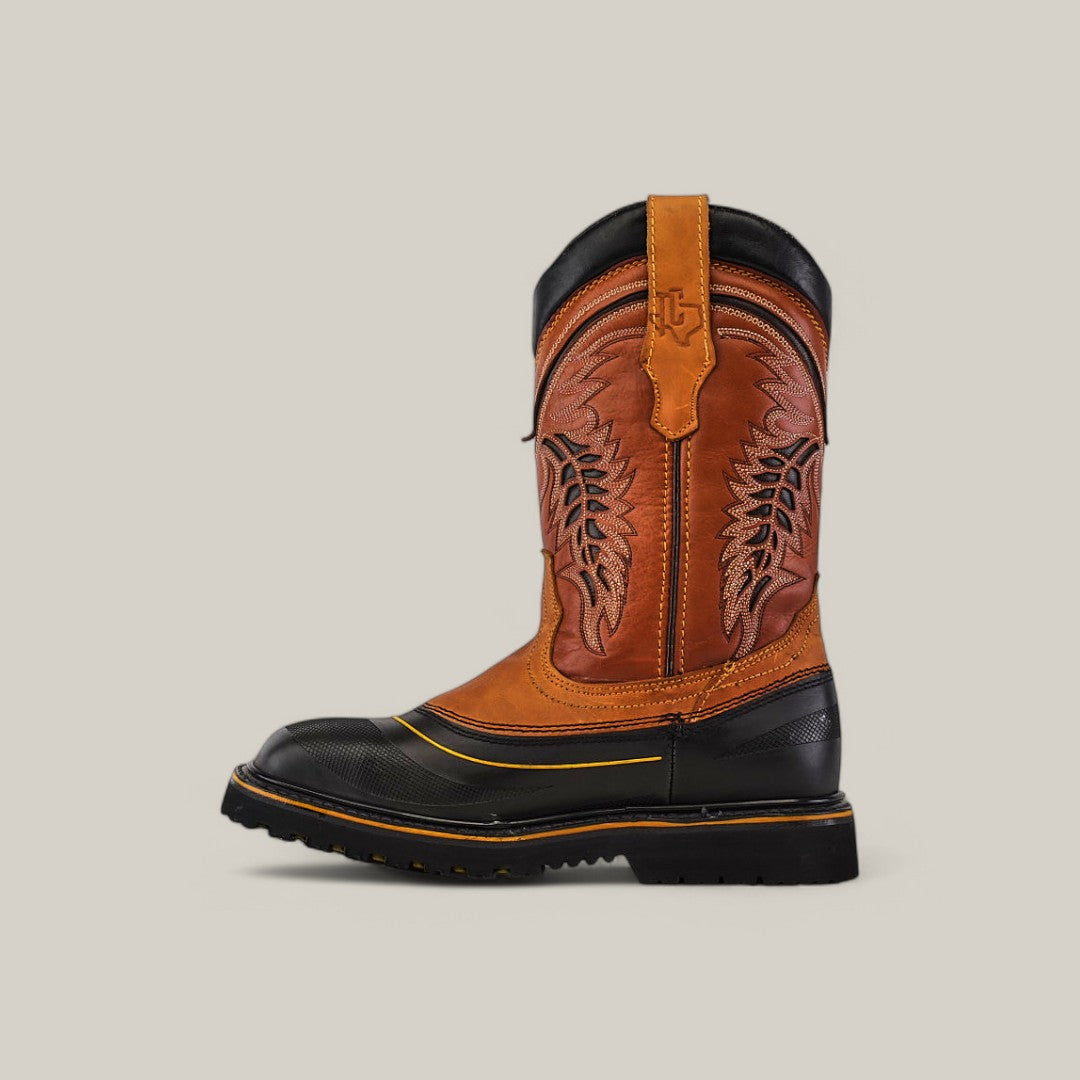 Side view of the Crazy Honey Soft Toe - E6048 Texas Country Work Boot, showcasing its brown leather upper with decorative stitching, black rubber sole, and toe cap. Known for its durability, it features pull-on loops and a subtle logo against a plain beige background.