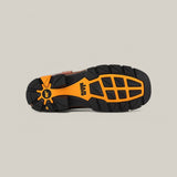 The image displays the sole of an Amazonas Cogñac Composite Toe - E6002 boot, featuring a rugged black design with orange accents. Geometric patterns ensure traction, and a logo is on the heel. Built for durability in tough conditions, its set against a light gray background.