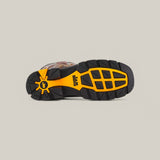 The image features the sole of the Amazonas Chocolate Soft Toe - E6002, a waterproof boot with rugged tread, perfect for Texas Country Work Boots. The black sole has orange accents and a logo with a stylized sun, set against a plain grayish background. It’s durable and comfortable on any terrain.