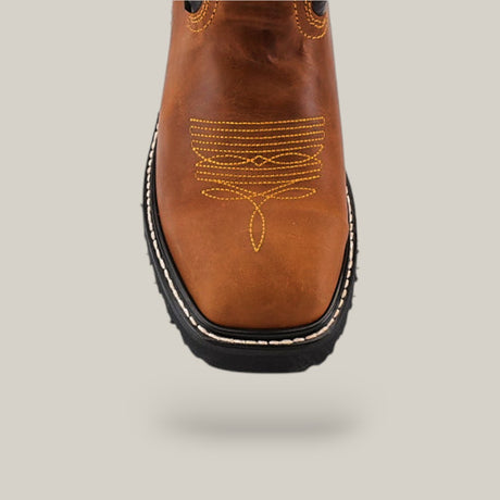 Close-up of the Golden Ateus Composite Toe - E6016, a rugged Texas Country Work Boot in brown leather with intricate yellow toe cap stitching. This durable boot features a black sole, white edge stitching, and is displayed against a plain light gray background to highlight its robust design.