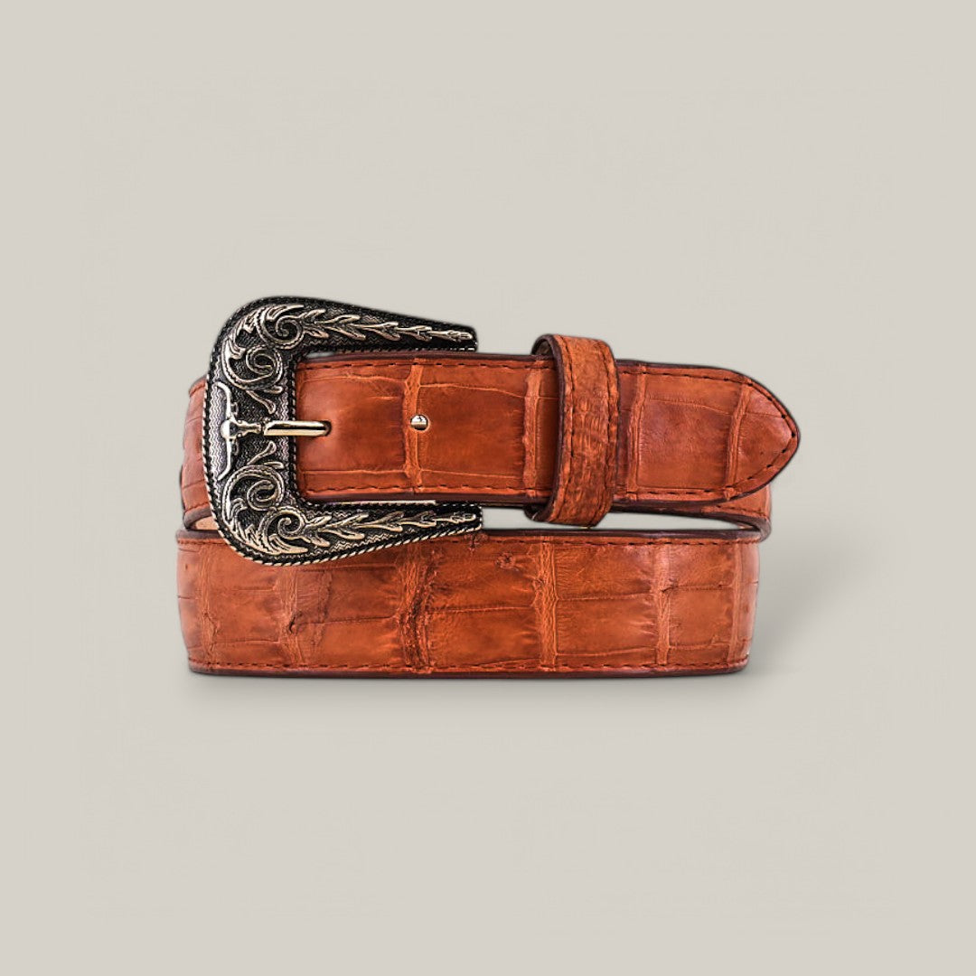 The Exotic Full Quilt Alligator - Texas Buckle - Brandy Belt, a luxury brown leather belt with a textured pattern and intricately designed decorative Texas buckle, is coiled neatly against a plain light gray background.