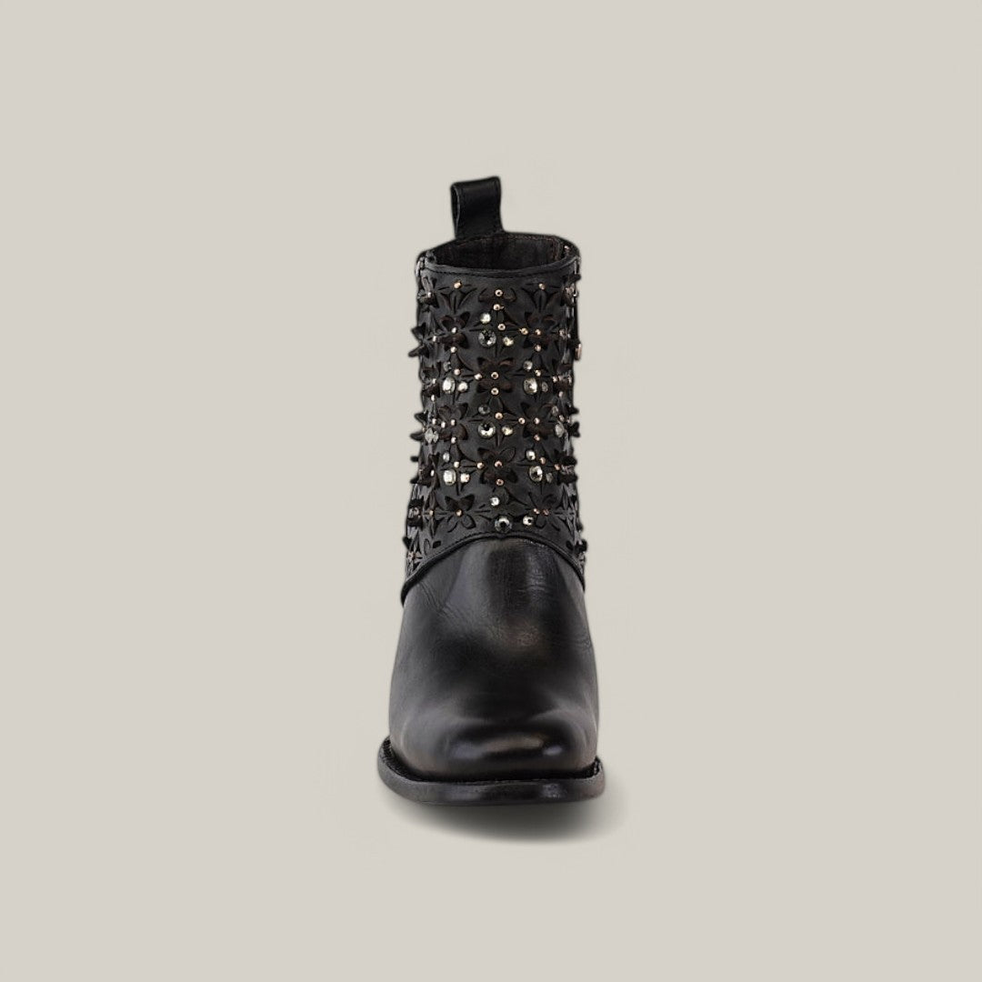 The Black Laser & Crystals - Round Toe - CU439 boot features floral cutouts and sparkling crystals set on a light gray backdrop, adorned with small round metal studs and a slightly elevated heel, blending elegance with glamour.