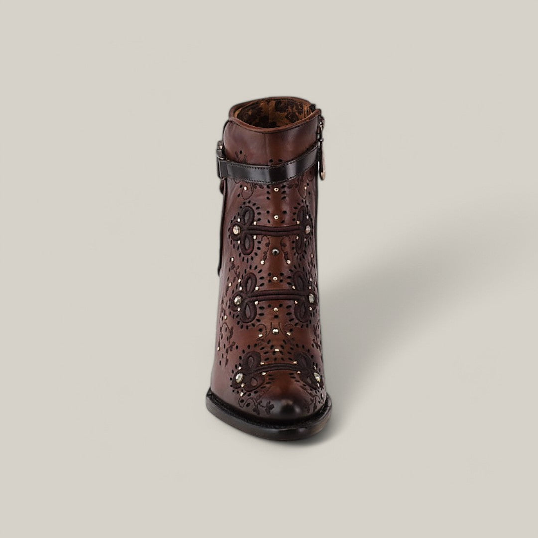 Front view of the Honey Embroidery & Studs & Harness - Round Toe - CU637, a brown ankle boot on a light gray background. It features decorative cut-out patterns, a stylish harness with black straps, a rounded toe, and intricate detailing enhanced by subtle studs for an artisanal look.