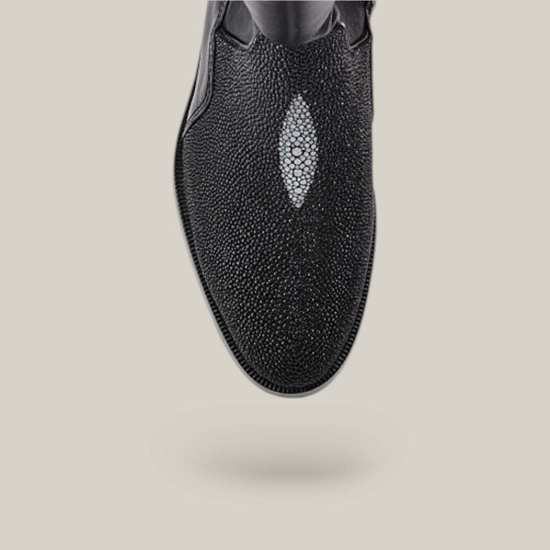 The Black Stingray Zipper - Round Toe (FC637) shoe, crafted from stingray leather, features a distinctive textured pattern and shiny oval detail on the upper. It stands elegantly against a soft beige background in this close-up shot.