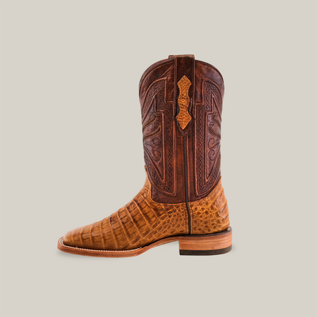 The Exotic Caiman Belly - Camel - Square Toe boot features a side profile with a brown leather upper, intricate stitching, and a lighter brown crocodile-patterned lower section. It has a sturdy flat heel and embossed shaft design, showcasing the elegance of exotic leather boots.