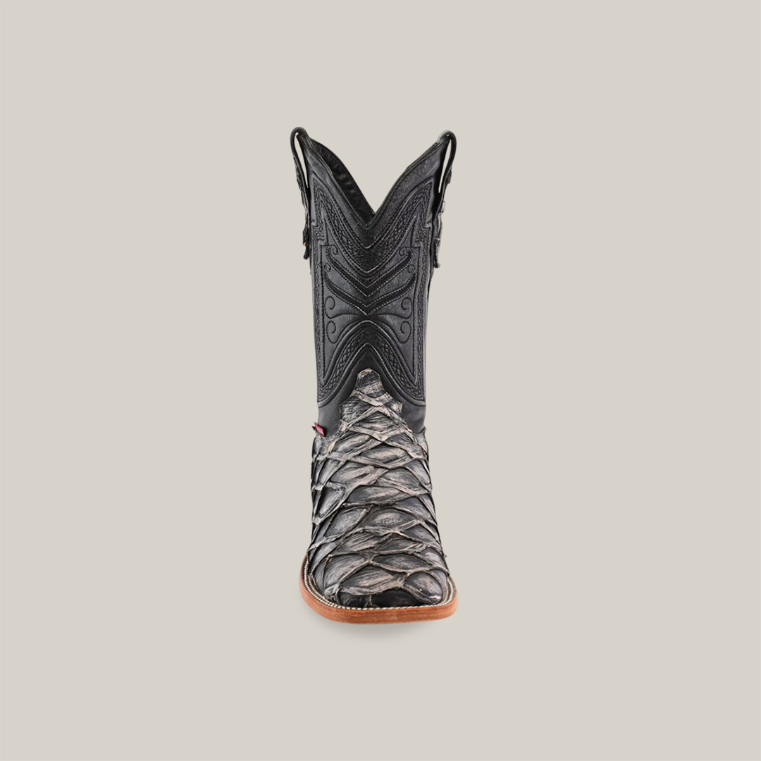 The Exotic Piraruco Fish - Rustic Bone boot showcases a scaly silver texture on the foot with intricate black stitching on the shaft, set against a plain light beige background.