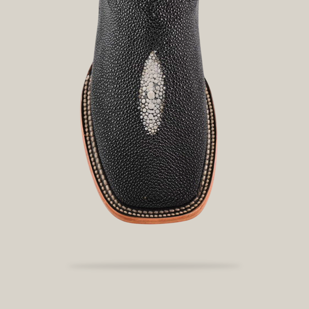 Close-up of the Exotic Stingray - Black - Square Toe cowboy boot, featuring an exotic texture with a decorative white spot, intricate edge stitching, and set against a plain light gray background.