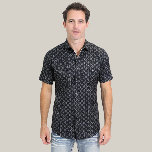 A man in the Mens Performance Western Short Sleeve Aztec Print Black Shirt (PGW10630) and light blue jeans stands against a plain gray background, looking directly at the camera.