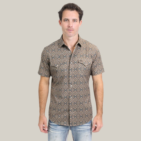 A man in the Mens Performance Western Short Sleeve Aztec Print Brown Shirt - PGW10638 and faded jeans stands against a plain backdrop, facing the camera.