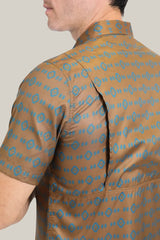 A person is wearing a Mens Performance Western Short Sleeve Aztec Print Camel Shirt - PGW10613, displayed from the side. The shirt showcases a blue Aztec print on brown fabric and features lightweight, breathable material with short sleeves and back fold detail.